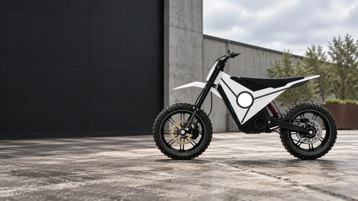 White electric off-road motorcycle with black battery housing and red rear shock photographed in an industrial courtyard