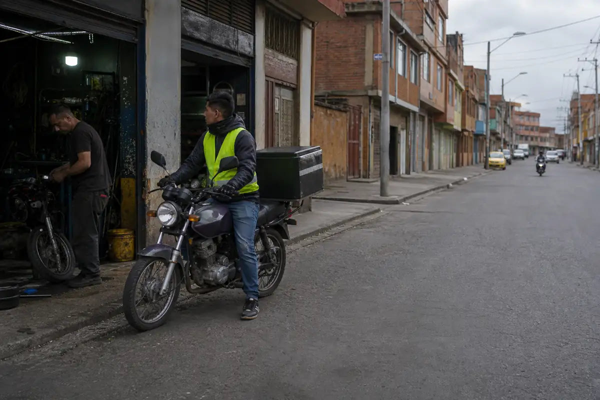 Colombia delivery rider on a commuter motorcycle outside an independent repair shop
